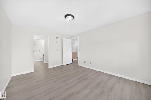 Spacious room with light wood-finish flooring, white baseboards, and a neutral wall color - #214 245 Edwards Dr Sw, Edmonton, AB - Indoor Photo Showing Other Room