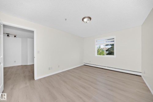 Room featuring wood-finish flooring, a contemporary ceiling light fixture, and a window with natural light - #214 245 Edwards Dr Sw, Edmonton, AB - Indoor Photo Showing Other Room