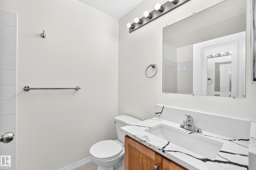 Bathroom featuring a wood-finish vanity with a built-in sink, a quartz-look countertop with black veining, an overhead vanity light fixture, and chrome hardware - #214 245 Edwards Dr Sw, Edmonton, AB - Indoor Photo Showing Bathroom