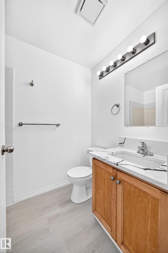 Bathroom featuring a wood-finish vanity with a white countertop and integrated sink, chrome faucet, and rectangular mirror - #214 245 Edwards Dr Sw, Edmonton, AB - Indoor Photo Showing Bathroom