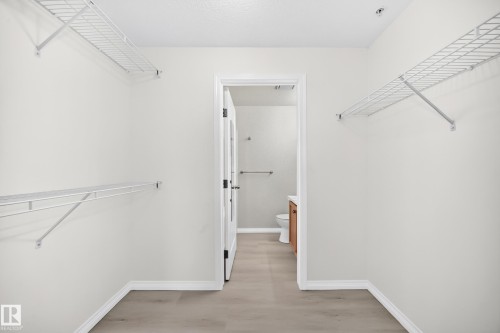 Walk-in closet featuring light wood-finish flooring, white wire shelving, recessed lighting, and a white paneled door with frosted glass inserts - #214 245 Edwards Dr Sw, Edmonton, AB - Indoor With Storage