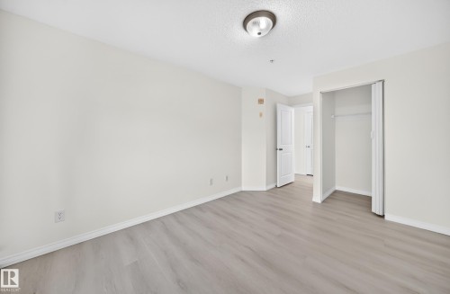 Spacious interior room featuring light wood-finish flooring, white baseboards, and neutral wall paint - #214 245 Edwards Dr Sw, Edmonton, AB - Indoor Photo Showing Other Room