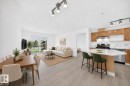 Open-concept living space featuring wood-finish flooring, a kitchen island with stone-finish countertop, stainless steel appliances, and a sliding glass door leading to a private patio - #214 245 Edwards Dr Sw, Edmonton, AB  - Indoor 