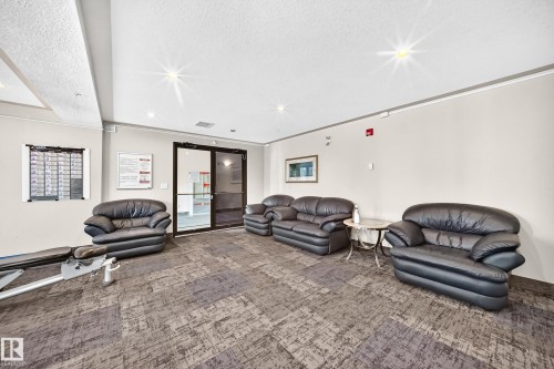 Entryway lounge featuring a patterned carpet, multiple dark leather sofas and armchairs, a glass-top side table, and double glass entry doors - #214 245 Edwards Dr Sw, Edmonton, AB - Indoor