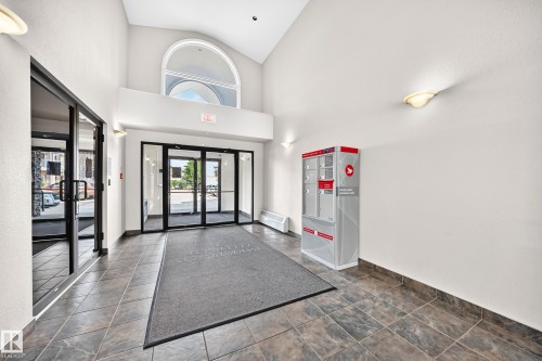 Building entryway featuring tile flooring, glass doors, and a vaulted ceiling with an arched window - #214 245 Edwards Dr Sw, Edmonton, AB - Indoor Photo Showing Other Room