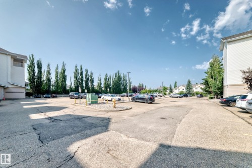 Paved parking area surrounded by residential buildings and mature trees - #214 245 Edwards Dr Sw, Edmonton, AB - Outdoor