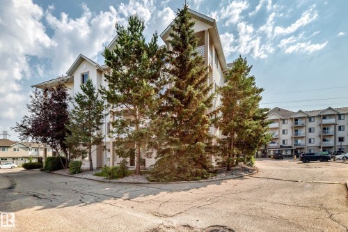 Multi-story residential building featuring light-colored siding and a pitched roofline - #214 245 Edwards Dr Sw, Edmonton, AB - Outdoor With Facade