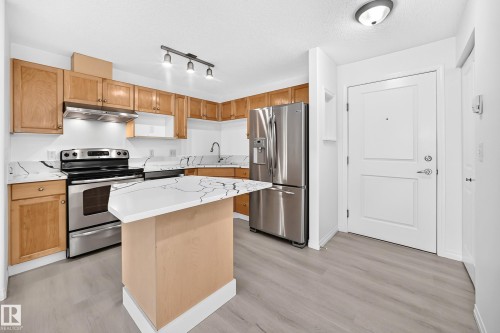 Kitchen featuring stainless steel appliances, light wood-finish cabinetry, patterned countertops, a peninsula with seating space, and light wood-finish flooring - #214 245 Edwards Dr Sw, Edmonton, AB - Indoor Photo Showing Kitchen