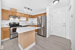 Kitchen featuring stainless steel appliances, light wood-finish cabinetry, patterned countertops, a peninsula with seating space, and light wood-finish flooring - 