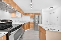 Kitchen featuring light wood cabinetry with brushed nickel hardware, white countertops with dark veining, stainless steel appliances, and light wood-finish flooring - 
