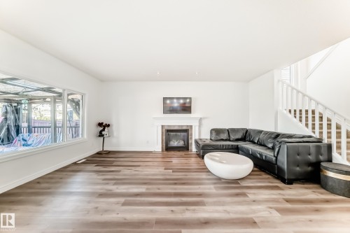 Spacious living area featuring wood-finish flooring, a contemporary fireplace with a white mantel and stone surround, and a large window - 2812 12 Street Nw, Edmonton, AB - Indoor Photo Showing Living Room With Fireplace
