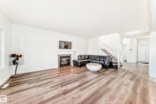 Spacious living area featuring wood-finish flooring, a white mantel fireplace with tile surround, and a visible staircase with white balusters - 2812 12 Street Nw, Edmonton, AB - Indoor Photo Showing Other Room With Fireplace