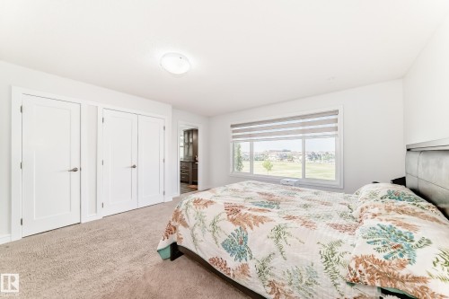 Light-filled room featuring a large window with horizontal blinds, neutral carpet flooring, and two sets of white panel doors - 2812 12 Street Nw, Edmonton, AB - Indoor Photo Showing Bedroom