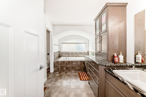 Bathroom featuring a built-in soaking tub with tiled surround, an arched window, and large format floor tiles - 2812 12 Street Nw, Edmonton, AB - Indoor