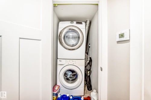 Dedicated laundry closet featuring a stacked white washer and dryer unit, white paneled door, and a wall-mounted thermostat - 2812 12 Street Nw, Edmonton, AB - Indoor Photo Showing Laundry Room
