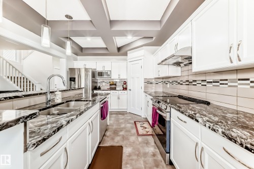 Modern kitchen featuring white cabinetry, stainless steel appliances, dark patterned countertops, a tile backsplash, and a coffered ceiling - 2812 12 Street Nw, Edmonton, AB - Indoor Photo Showing Kitchen With Double Sink With Upgraded Kitchen