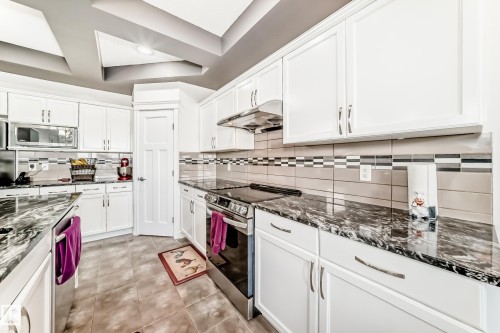 Kitchen featuring white cabinetry, dark polished countertops, and a tiled backsplash with decorative accents - 2812 12 Street Nw, Edmonton, AB - Indoor Photo Showing Kitchen With Upgraded Kitchen