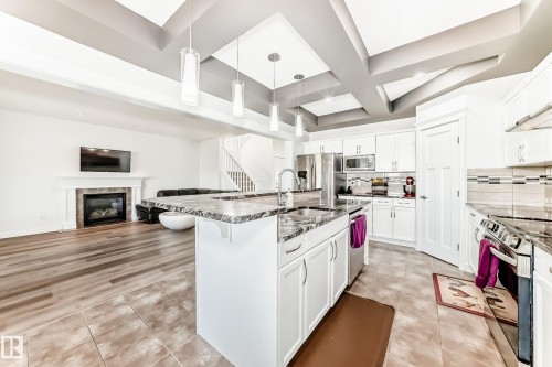 Modern kitchen featuring white cabinetry, stainless steel appliances, and a large central island with a sink and stone-finish countertop - 2812 12 Street Nw, Edmonton, AB - Indoor Photo Showing Kitchen