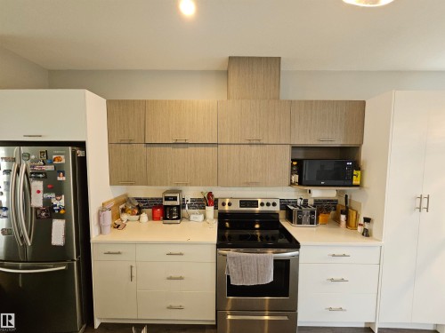 Modern kitchen featuring stainless steel French door refrigerator, black electric range with convection oven, and dual-tone cabinetry combining cream-finished lower cabinets with natural wood-finish uppers - 15212 98 Avenue Nw, Edmonton, AB - Indoor Photo Showing Kitchen