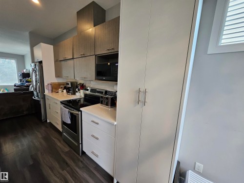 Kitchen featuring wood-finish flooring, white cabinetry, integrated stainless steel appliances, and a tiled backsplash - 15212 98 Avenue Nw, Edmonton, AB - Indoor Photo Showing Kitchen