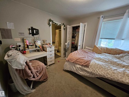 Carpeted room featuring a window with blinds, a built-in closet with double doors, and an open doorway - 15212 98 Avenue Nw, Edmonton, AB - Indoor Photo Showing Bedroom