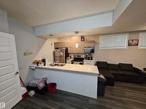 Kitchen island with a light-toned countertop, stainless steel refrigerator, stainless steel range, and wood-finish cabinetry - 15212 98 Avenue Nw, Edmonton, AB - Indoor Photo Showing Other Room