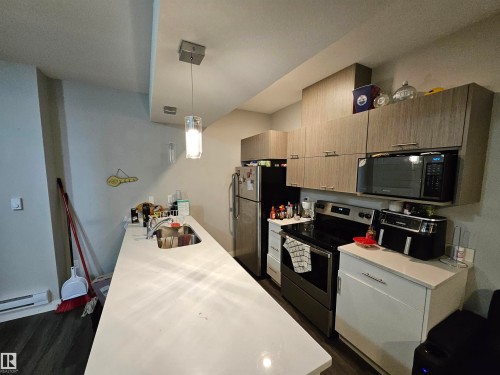 Kitchen featuring wood-finish cabinetry, stainless steel appliances, a built-in microwave, and a white countertop with an integrated sink - 15212 98 Avenue Nw, Edmonton, AB - Indoor Photo Showing Kitchen