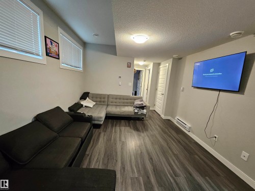 Wood-finish flooring, two windows with blinds, wall-mounted television, and a built-in baseboard heater - 15212 98 Avenue Nw, Edmonton, AB - Indoor