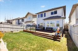 Expansive backyard featuring a manicured lawn, a multi-level wood deck with glass panel railing, and a vinyl-sided exterior with multiple windows - 