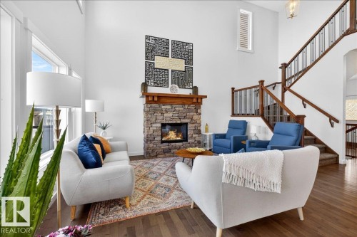 Two-story living area featuring a stone-faced fireplace with wood mantel, hardwood flooring, and a multi-level staircase with wood railings - 3936 Claxton Loop Sw, Edmonton, AB - Indoor Photo Showing Living Room With Fireplace