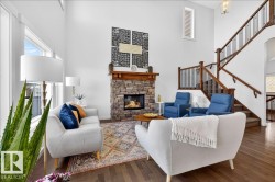 Two-story living area featuring a stone-faced fireplace with wood mantel, hardwood flooring, and a multi-level staircase with wood railings - 