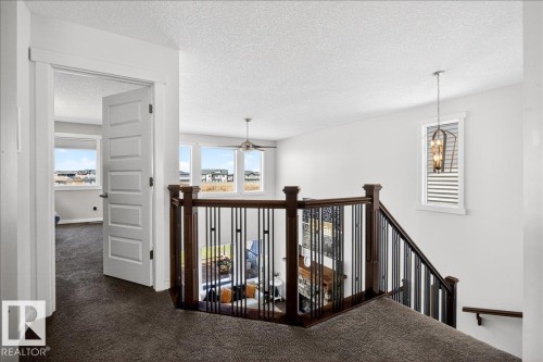 Open upper-level landing with dark wood and wrought iron railing, white paneled doors, and a decorative pendant light fixture - 3936 Claxton Loop Sw, Edmonton, AB - Indoor Photo Showing Other Room