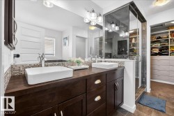 Spa-inspired primary bathroom featuring dual vessel sinks with wood-finish vanity cabinetry, quartz countertops with mosaic tile backsplash, chrome fixtures, and large-format mirror with integrated lighting - 
