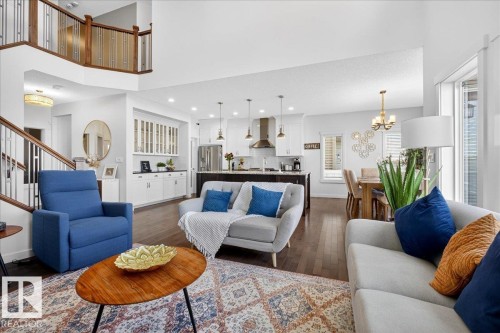 Open-concept living area featuring wood-finish flooring, a two-story entryway, and a prominent staircase with wood and metal railing - 3936 Claxton Loop Sw, Edmonton, AB - Indoor Photo Showing Living Room