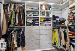 Spacious walk-in closet featuring floor-to-ceiling custom cabinetry with multiple shelving sections, organized storage drawers, and dual hanging rods for efficient wardrobe organization - 