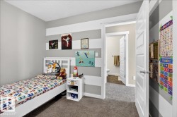 Bright bedroom featuring carpet flooring, built-in wall shelving with display niches, a white wood-finish bed frame, and bedside storage cabinet - 