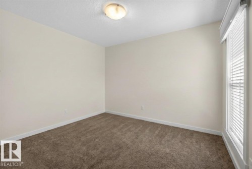 Neutral-toned walls, textured ceiling, flush mount lighting, brown carpeting, and a window with blinds - 3936 Claxton Loop Sw, Edmonton, AB - Indoor Photo Showing Other Room