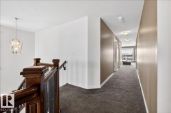 Hardwood newel posts with dark balusters, textured carpet flooring, and a modern pendant light fixture - 