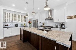 Kitchen featuring a central island with a built-in sink, stainless steel appliances, white cabinetry, and wood-finish flooring - 