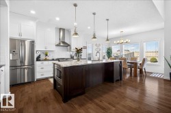 Gourmet kitchen featuring stainless steel French-door refrigerator and gas range with hood ventilation, white cabinetry with brushed nickel hardware, quartz countertops, and a substantial dark wood-finish island with pendant lighting - 