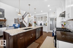 Chef's kitchen featuring a substantial dark wood island with light stone countertops, professional-grade gas range with stainless steel hood, white cabinetry with glass-front uppers, recessed lighting, and brass pendant fixtures - 