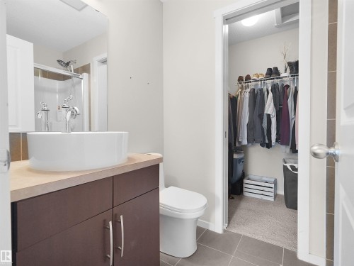 Modern vessel sink, wood-finish vanity, chrome fixtures, tile flooring, and a walk-in closet - #89 603 Watt Bv Sw, Edmonton, AB - Indoor Photo Showing Bathroom