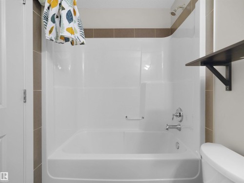 White bathtub with integrated shower, chrome fixtures, and neutral-toned wall tiles - #89 603 Watt Bv Sw, Edmonton, AB - Indoor Photo Showing Bathroom