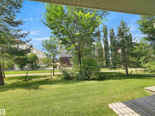 Expansive backyard featuring a manicured lawn, mature trees, and a partial wooden deck - #89 603 Watt Bv Sw, Edmonton, AB - Outdoor