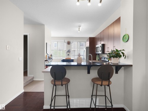 Kitchen featuring wood-finish flooring, dark-toned cabinetry, stainless steel appliances, and an eat-at counter with seating - #89 603 Watt Bv Sw, Edmonton, AB - Indoor Photo Showing Kitchen
