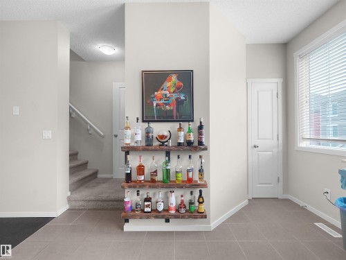 Recessed wall shelving with wood finish, large window with blinds, tile flooring, and carpeted staircase - #89 603 Watt Bv Sw, Edmonton, AB - Indoor Photo Showing Other Room