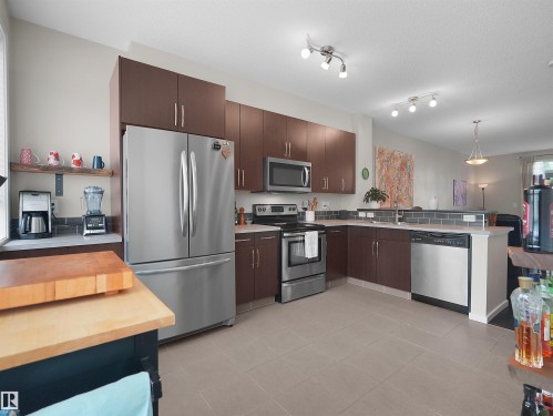 Sleek kitchen featuring stainless steel appliances, dark wood-finish cabinetry, tile flooring, and a gray subway tile backsplash - #89 603 Watt Bv Sw, Edmonton, AB - Indoor Photo Showing Kitchen With Stainless Steel Kitchen