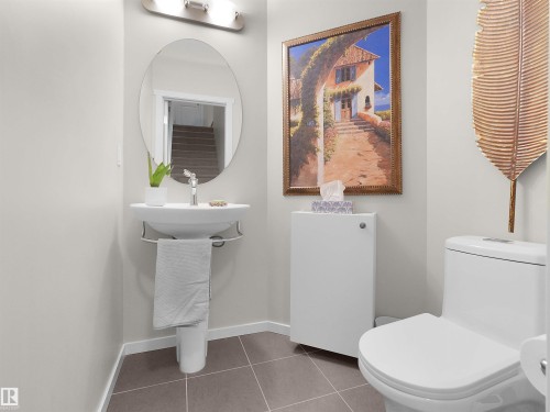 Pedestal sink with chrome faucet, oval mirror, wall-mounted light fixture, and tile flooring - #89 603 Watt Bv Sw, Edmonton, AB - Indoor Photo Showing Bathroom