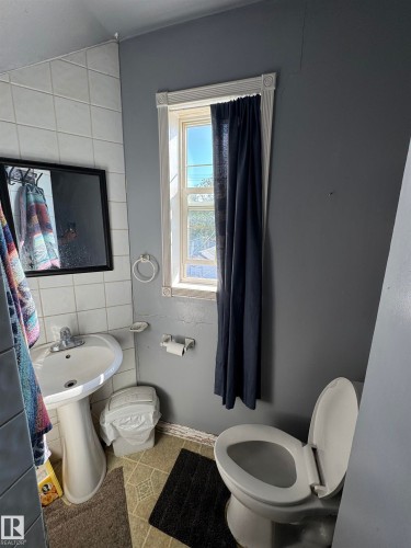 Functional bathroom featuring dual fixtures, pedestal sink with chrome hardware, tile wall surround, and natural light from window with dark curtain treatment - 11147 97 Street Nw, Edmonton, AB - Indoor Photo Showing Bathroom