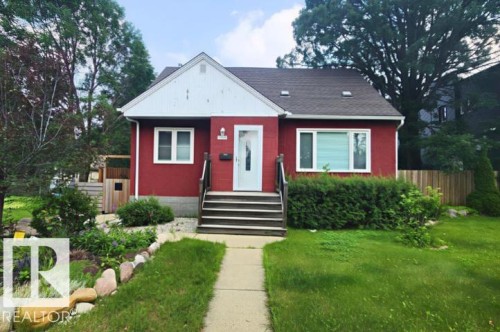Red exterior with white trim, dark shingle roof, concrete walkway, and landscaped front yard with mature plantings and stone accents - 11011 135 Street Nw, Edmonton, AB 